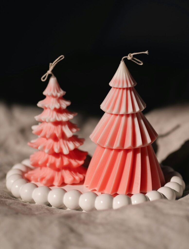 Two pink Christmas tree-carved cylindrical candles on a small white round tray with a rim carved like a strand of large pearls.