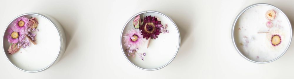 Soy candles, like the ones shown in the photo here, are the most common clean burning candles. These soy candles, seen close-up and from a top-down view, are poured in small metal tins with tiny dried purple-hued flowers on top, surrounding wood wicks
