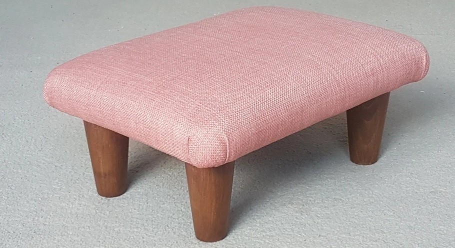 Close-up photo of a comfortable footstool with wooden legs, upholstered in a salmon pink fabric