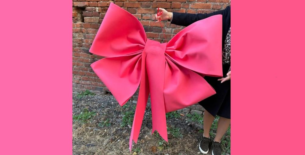 A person holds up a giant pink-coloured bow.
