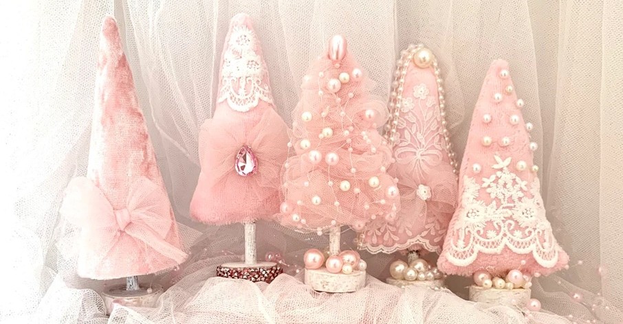 Close-up photo of five small pink Christmas tree decorations made of soft materials and fabrics and embellished with pearls, jewels, white lace, etc.