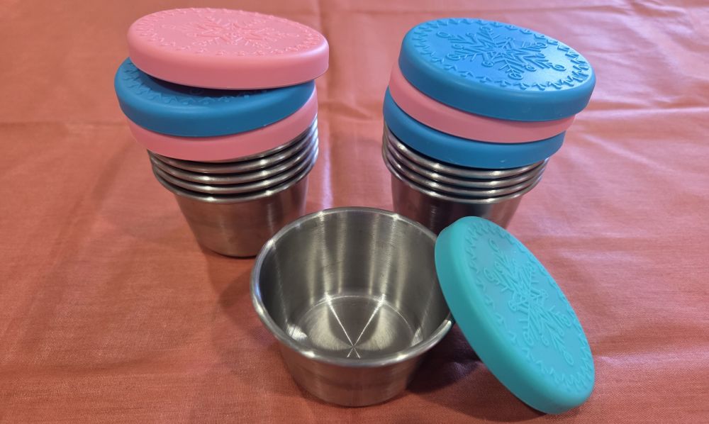 A couple of stacks of stainless steel mini food containers with multiple coloured silicone lids stacked on top, in blues and pink