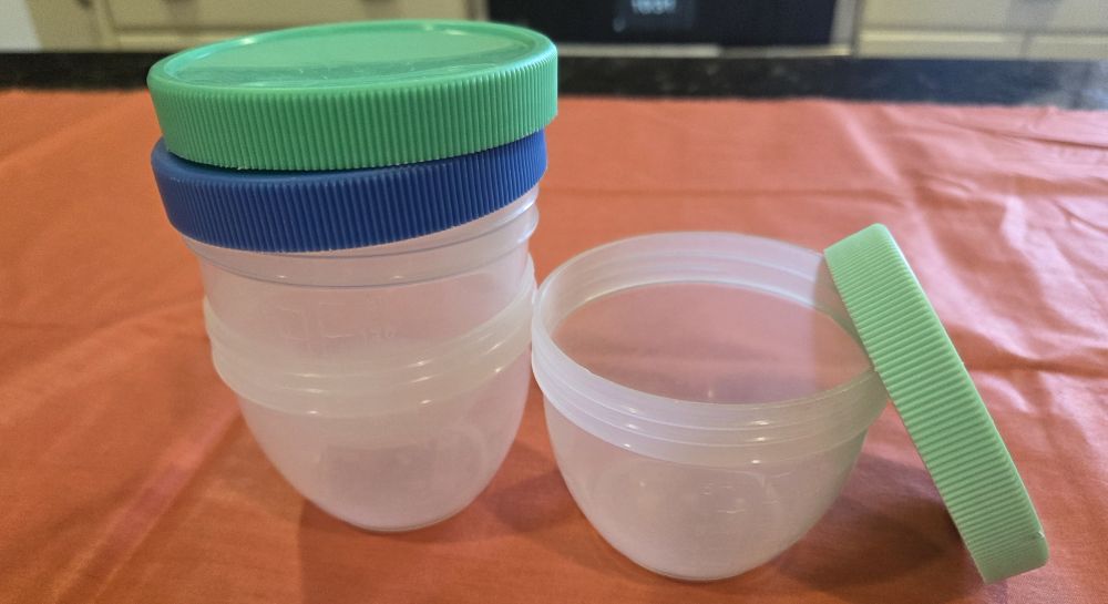 A few stacked small clear plastic food storage containers with blue and sea green lids stacked on top