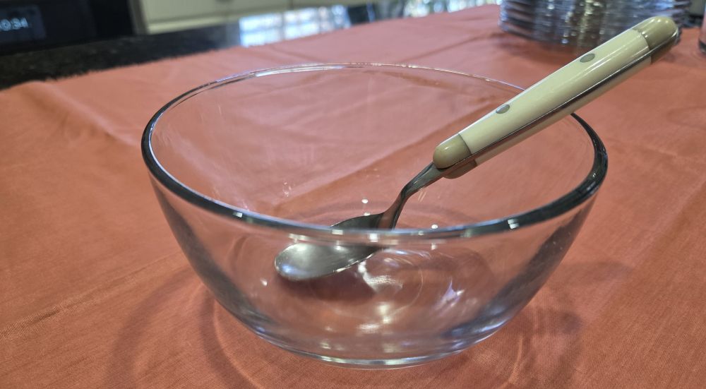 Close-up photo of a clear glass bowl with a spoon resting inside. Healthy household products include glass serveware such as this.