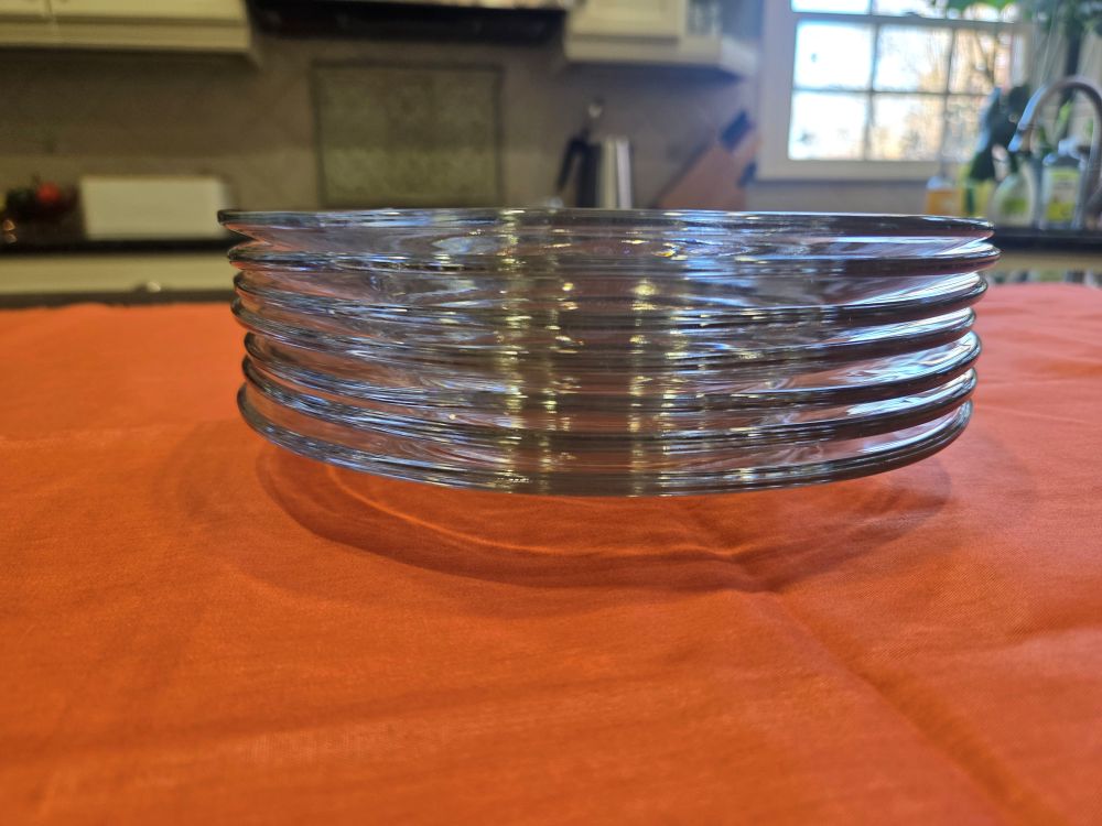A stack of clear glass plates viewed from the side atop a counter covered in coral-coloured cloth. Non-toxic household products include glass dishes like this.