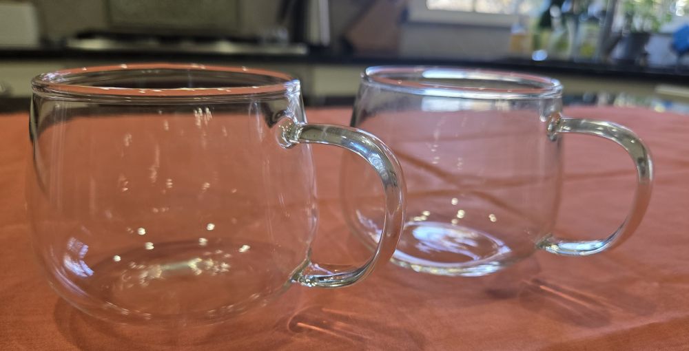 Two clear glass teacups are positioned side by side on a coral-coloured fabric spread over a kitchen counter. Such toxin-free household products are part of a serveware collection for which health is priority.