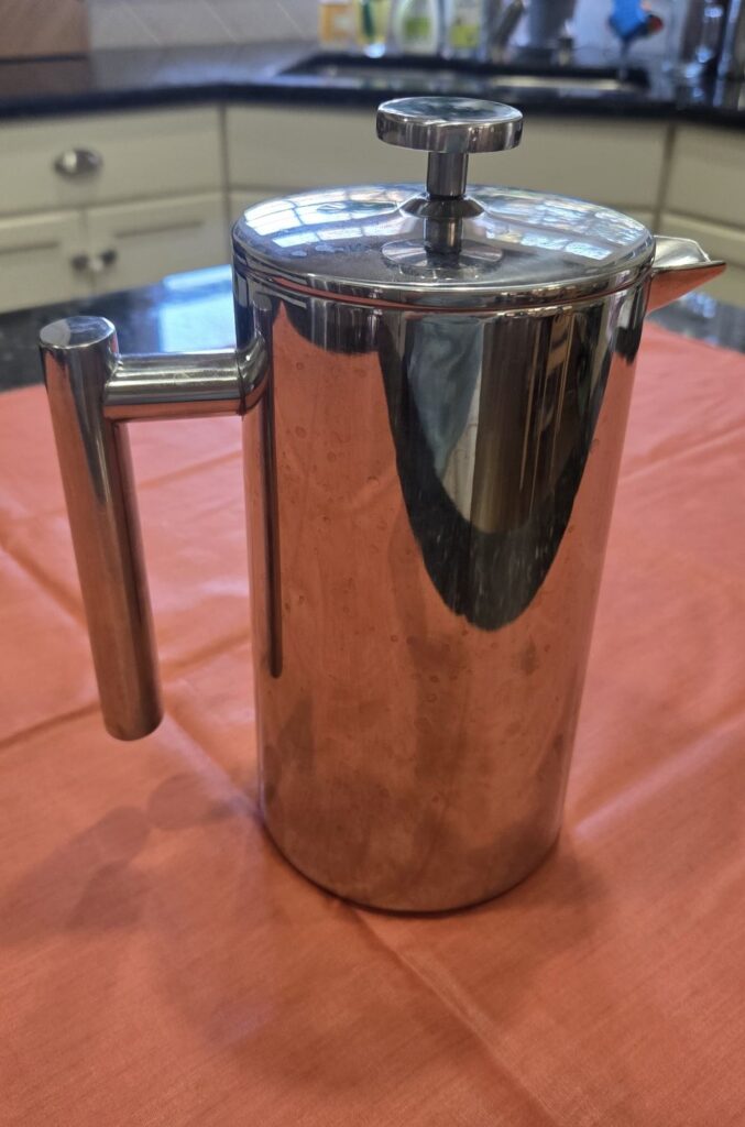 A 34-ounce stainless steel coffee press sits on a coral fabric swath on a kitchen counter. Household products used to prepare hot beverages such as this coffee press should always be made out of clear glass or stainless steel