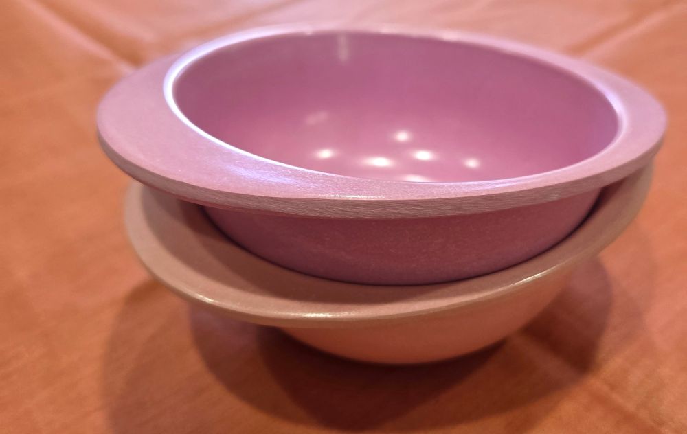 Close-up photo of two nested toddler bowls made out of bamboo, in pink and orange