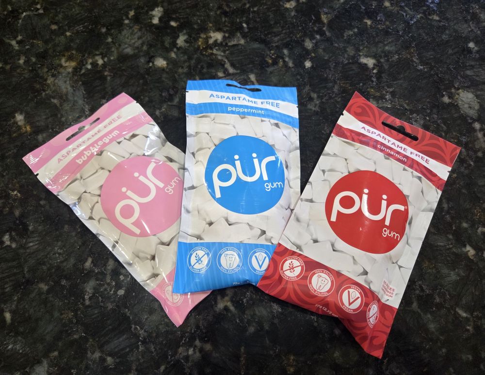 Three packets of pur gum arrayed atop a kitchen counter, in bubblegum, peppermint, and cinnamon flavours