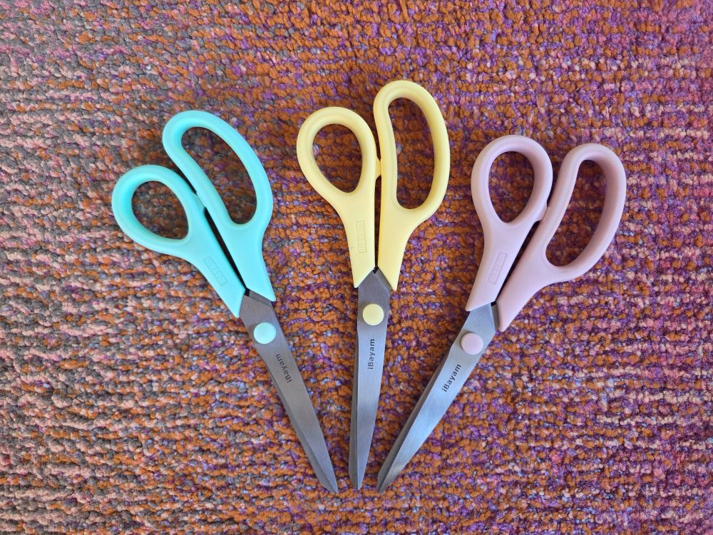 Three pairs of pastel kitchen scissors arrayed on colourful rug, in sea green, pale yellow and pale pink. If you need any given household products (such as scissors), opt for pretty versions like these!