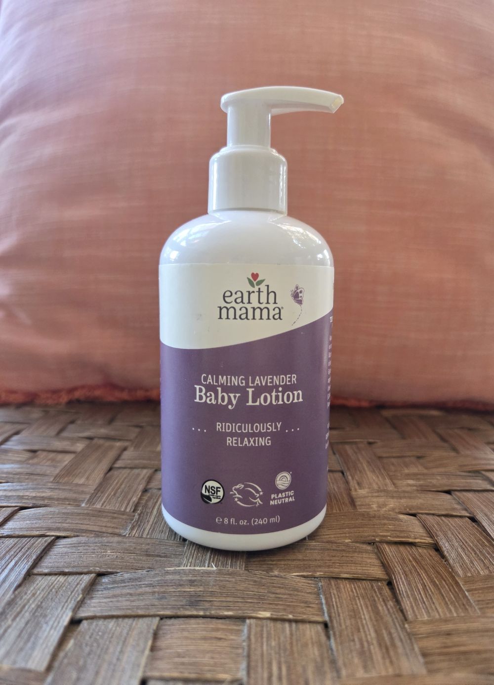 Bottle of Earth Mama lavender baby lotion atop a wicker chair in front of a coral pillow