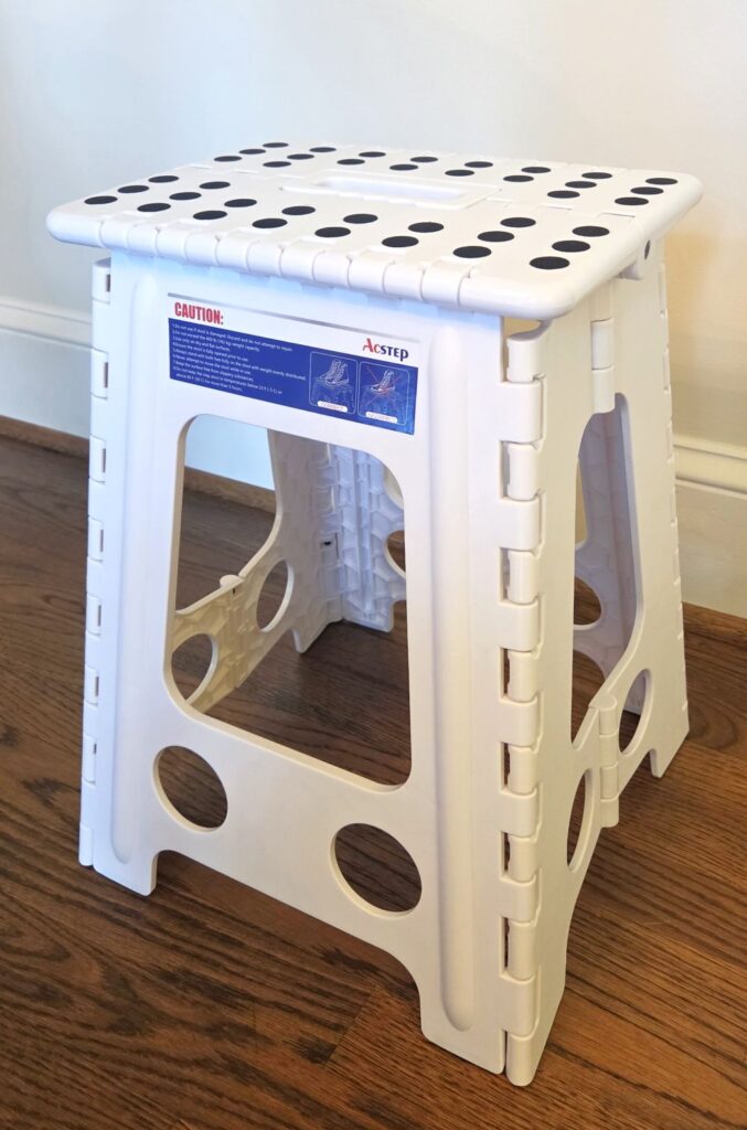 A white stepstool with grippy black circles/dots design stands assembled in front of a wall