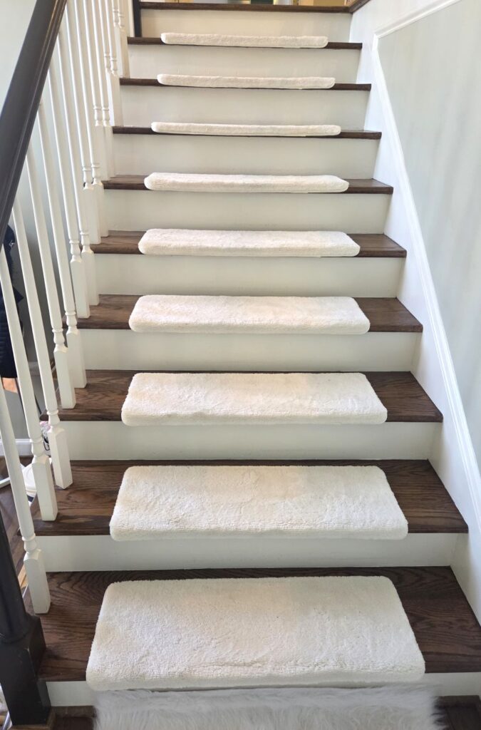 The upper half of a flight of stairs as seen from standing at the landing halfway up, with each step covered in comfortable off-white plush carpet stair treads
