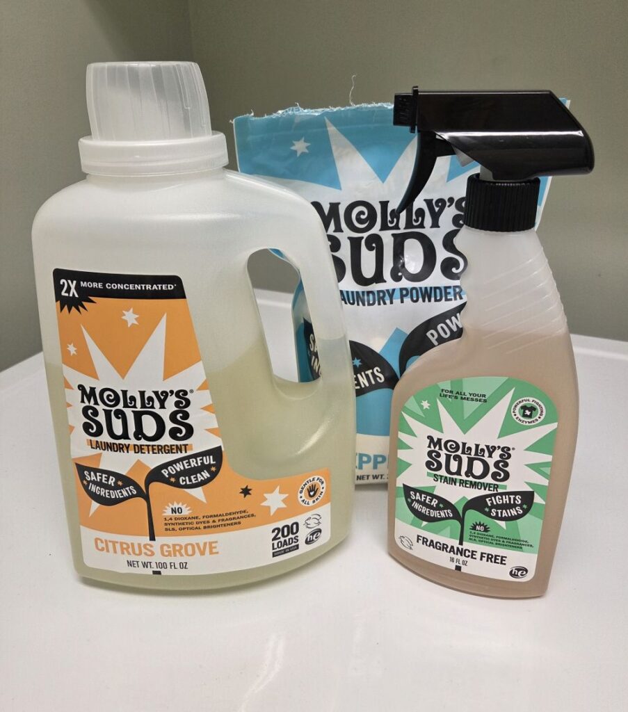 Molly's Suds liquid laundry detergent, powder laundry detergent, and laundry stain remover atop washing machine