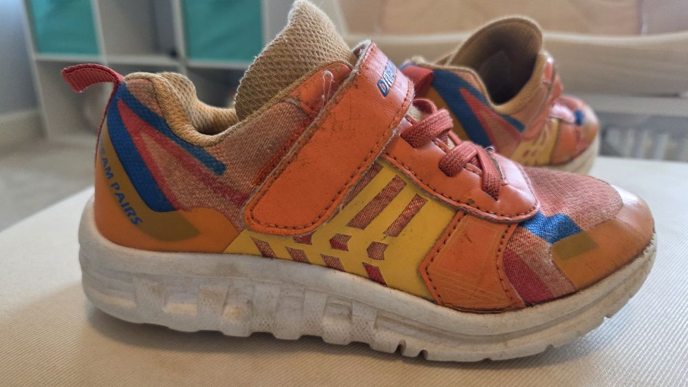 Close-up view of an orange pair of children's Dream Pairs athletic sneakers with Velcro straps (and non-functional/decorative laces). The white bottom of shoe is thick and ergonomically-shaped for safe and comfortable movement