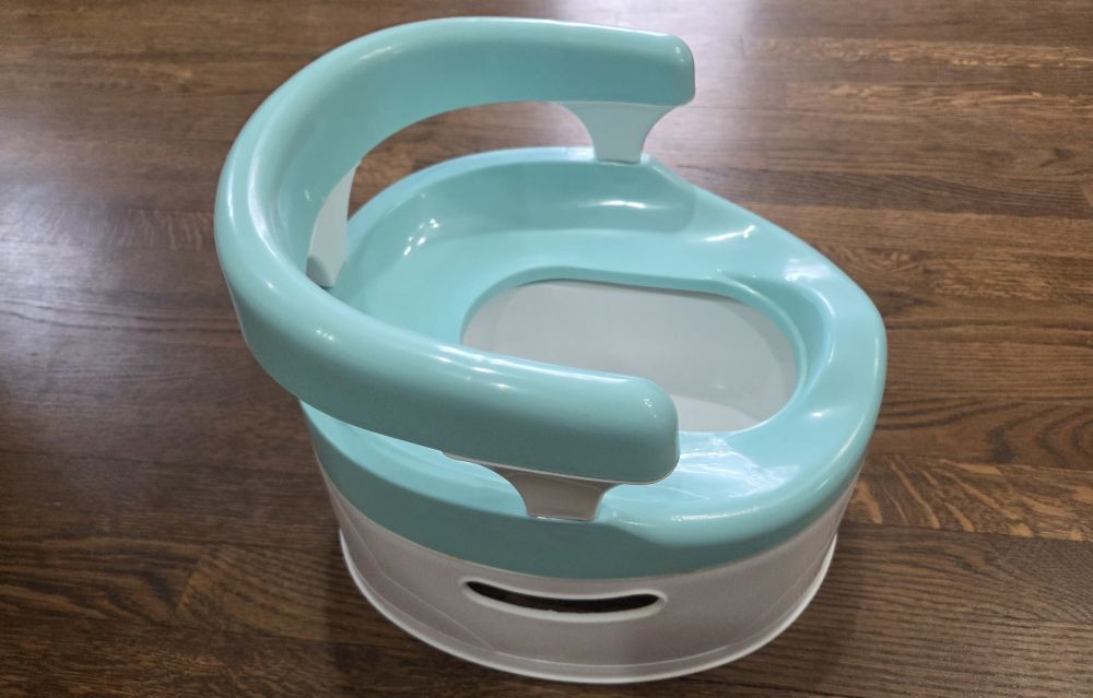 A white and aqua-coloured free-standing toddler toilet sits on a wood floor