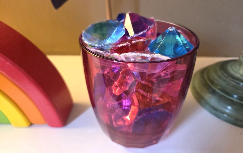 A clear pink plastic cup sits atop a shelf filled with many multi-coloured toy acrylic diamonds