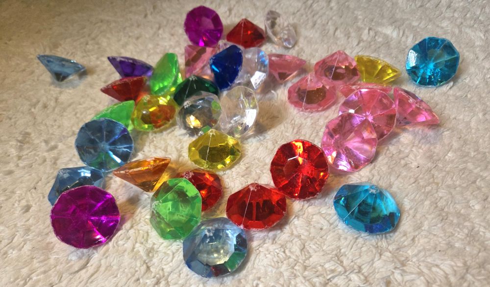 Dozens of colourful acrylic diamonds lay strewn about a rug, reflecting the light to 'sparkle'