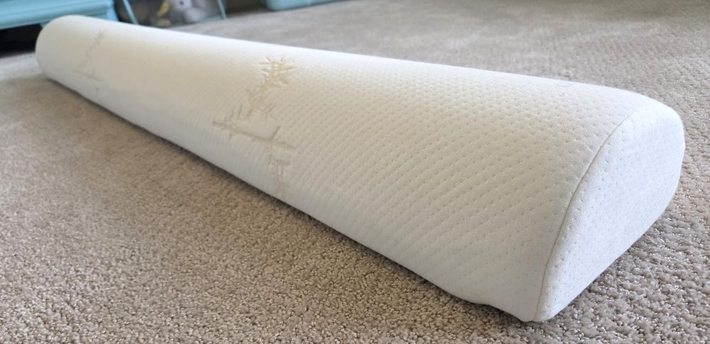 Close-up/diagonal front/side view of a long '3D half-circle' shaped bolster pillow/toddler bed rail with a soft white removable/washable cover, its texture visible up-cose