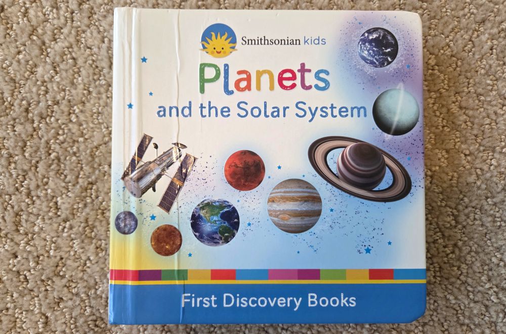 Top-down view of the cover of a baby/toddler board book called 'Planets and the Solar System' by Smithsonian Kids.
