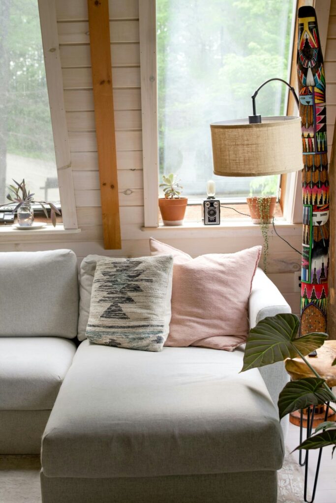 A corner sofa with comfy cushions and natural-textured floor lamp among other natural decor with shiplap wall and windows
