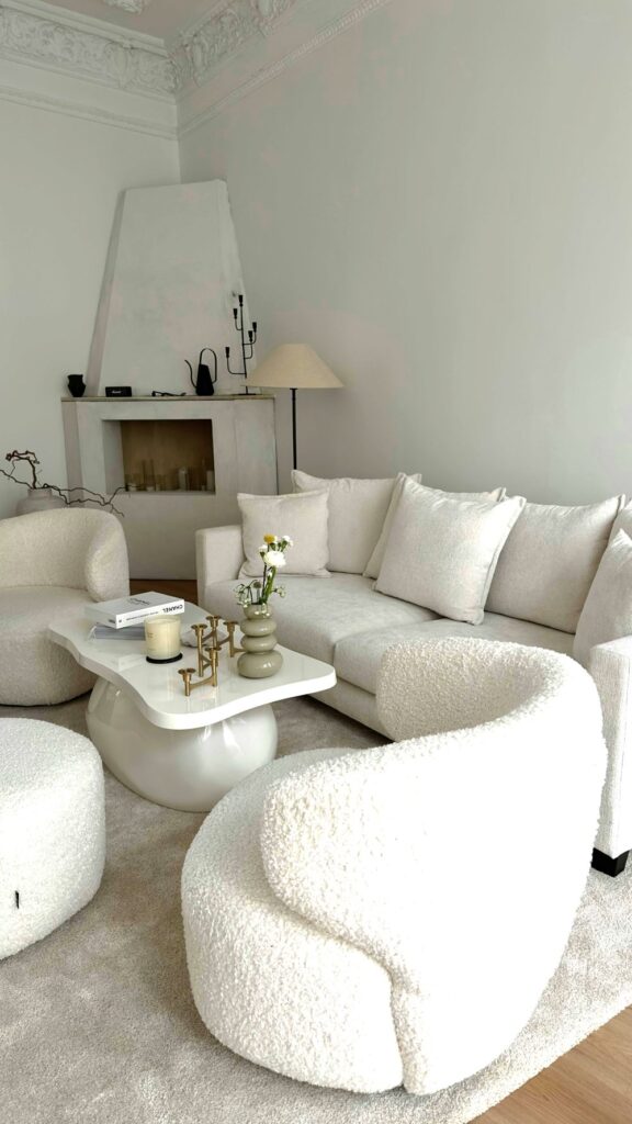 A very white living space is simply furnished with extra-soft upholstered chairs and sofa with matching cushions