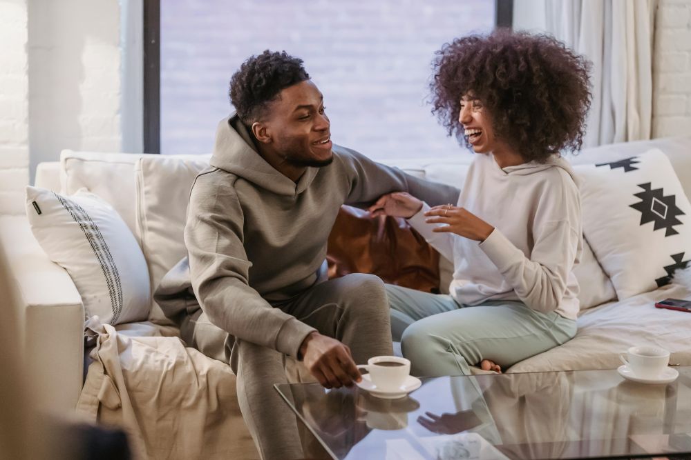 A couple happily relaxes on a comfortable sofa covered in cushions and a blanket with cappuccinos on the coffee table in front of them