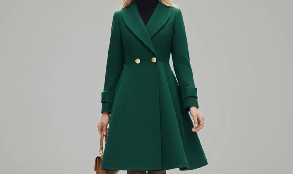 Close-up photo of an emerald green pea coat fitted at the waist worn by a woman holding a tan handbag. Two round gold buttons are seen on the front of the waist