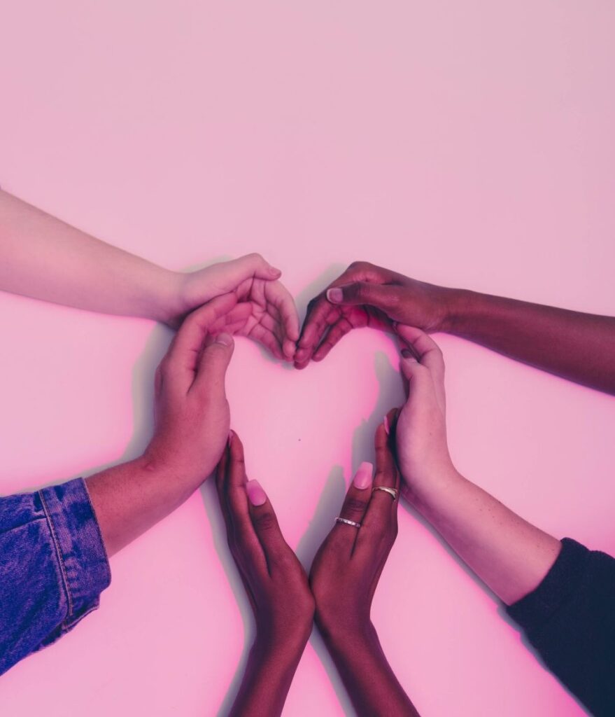 Three sets of hands are seen making the shape of a heart against a light pink background, a symbol of pure platonic February love