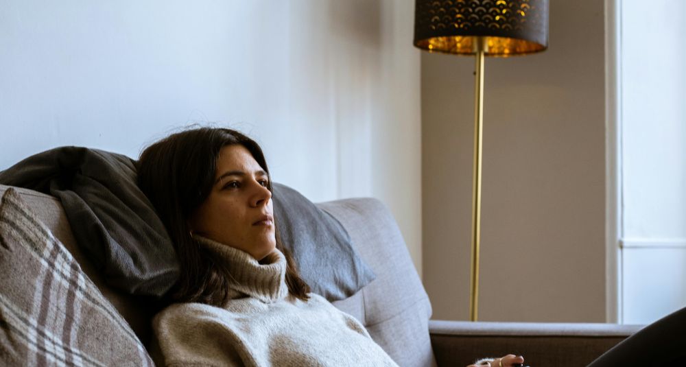 A woman sits on a sofa with a vacant and uninterested expression