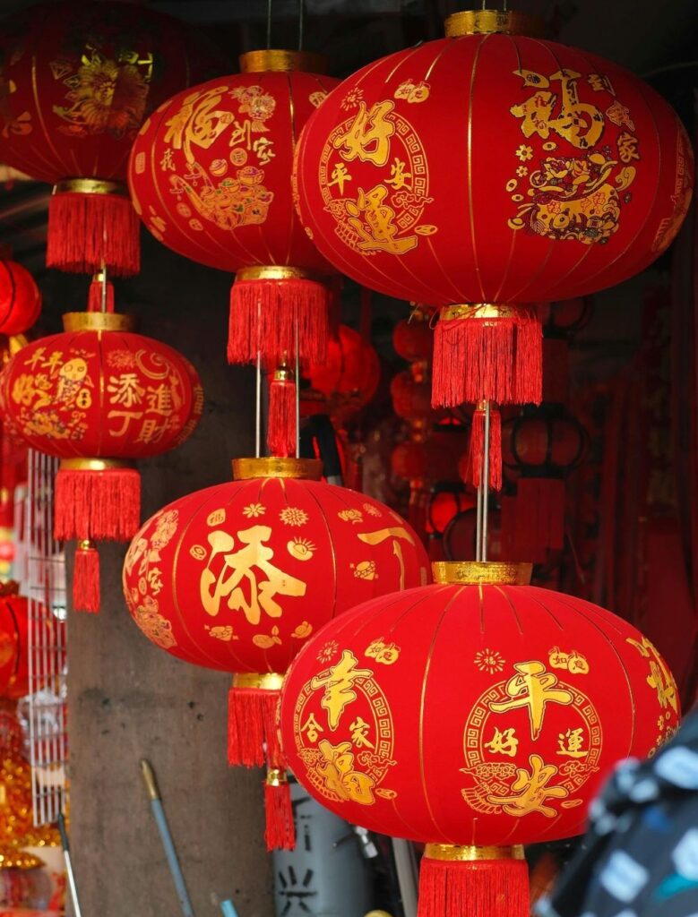 Several hanging bright red Chinese New Year lanterns with decorative gold Chinese letters and embelishments
