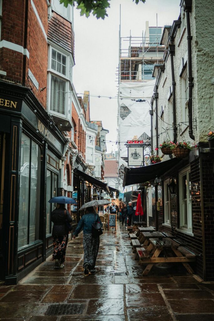 Photo of a quaint alley on a rainy day in Richmond, England with people seen in distance holding umbrellas