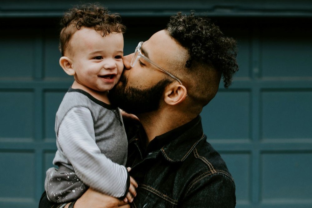 Close-up photo of a dad holding his smiling baby boy and kissing him. February love includes not just romance but the pure, unconditional love for children