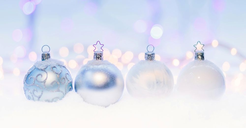Close-up view of four pearly white and satin light blue frosty glittery glass ball ornaments lined up in a row over fake snow