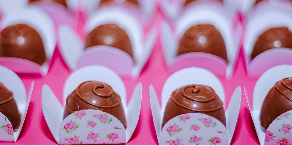 Close-up view of rows of delicious-looking chocolate truffles topped with swirled detail, each inside a tiny paper tray adorned with little pink roses