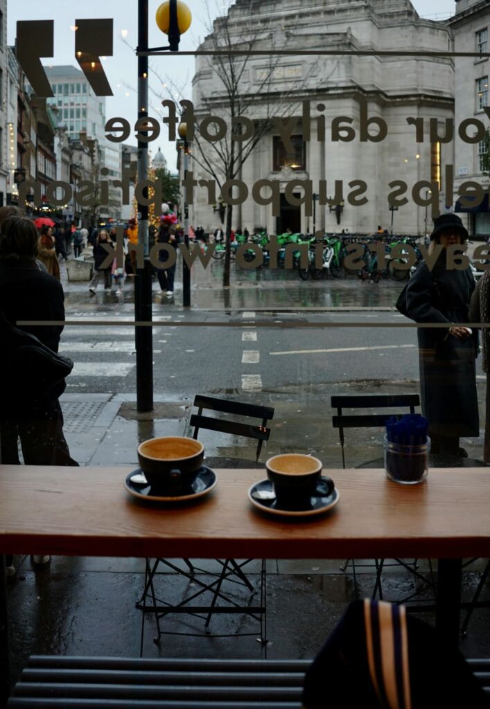 View as seen from inside a cosy cafe in London looking out the window at the rainy street. February love includes taking time to savor simple comforts like a latte inside a warm cafe on a cold day