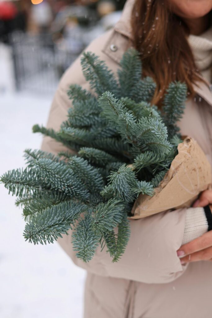 Close-up view of a woman in a warm coat clutching a bundle of evergreen branches outside