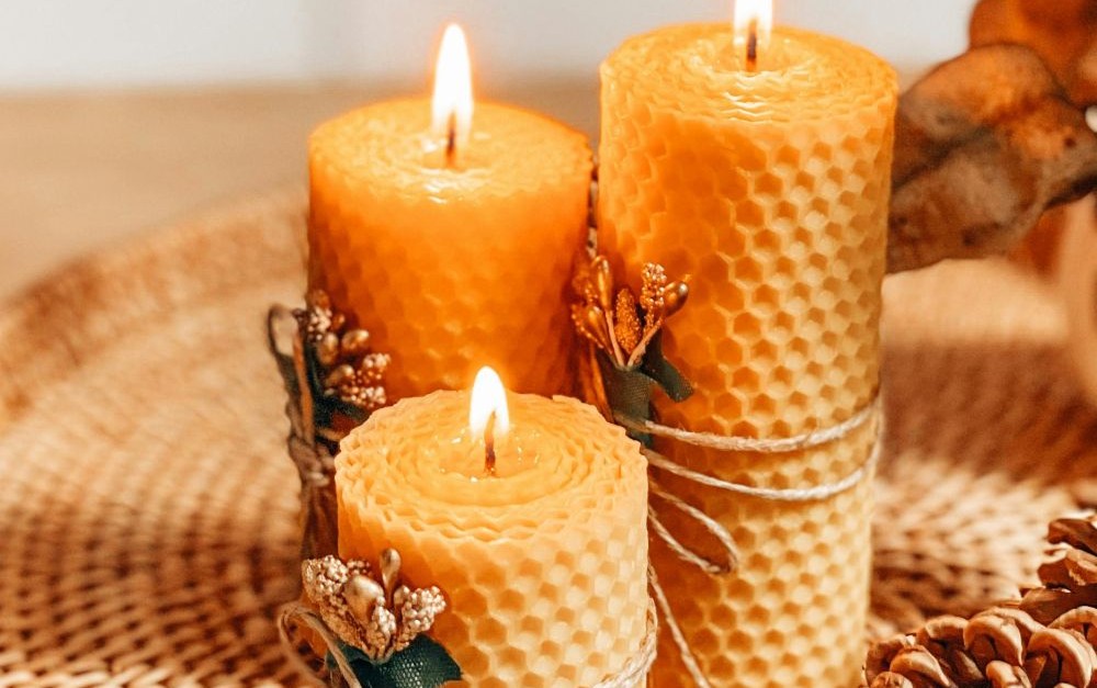 Close-up view of winter-themed candle scene with three lit beeswax pillar candles with honeycomb-indented edges and tied with twine and small gold-painted sparkly mistletoe sprigs