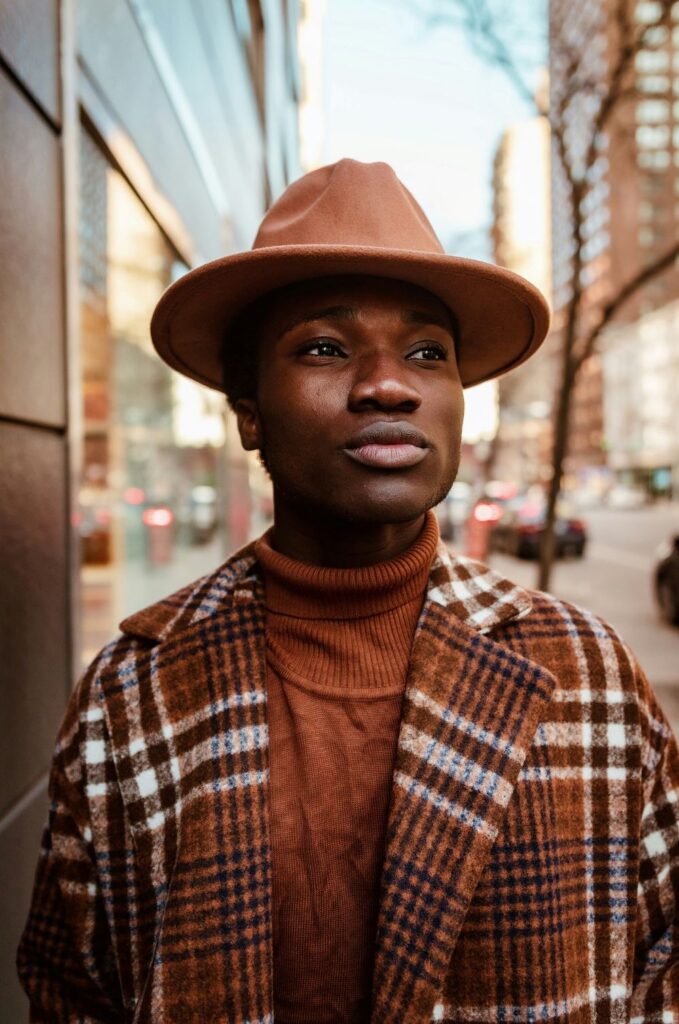Close-up photo of a man wearing a camel bowler hat with matching brown turtleneck and brown and tan plaid coat