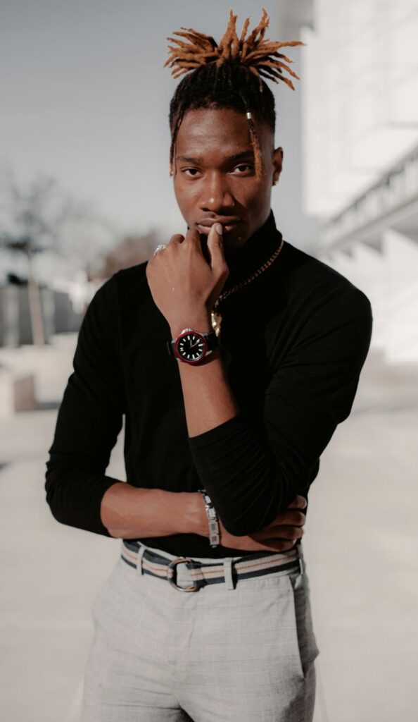 A man poses in a fitted black turtleneck, gray slacks and belt