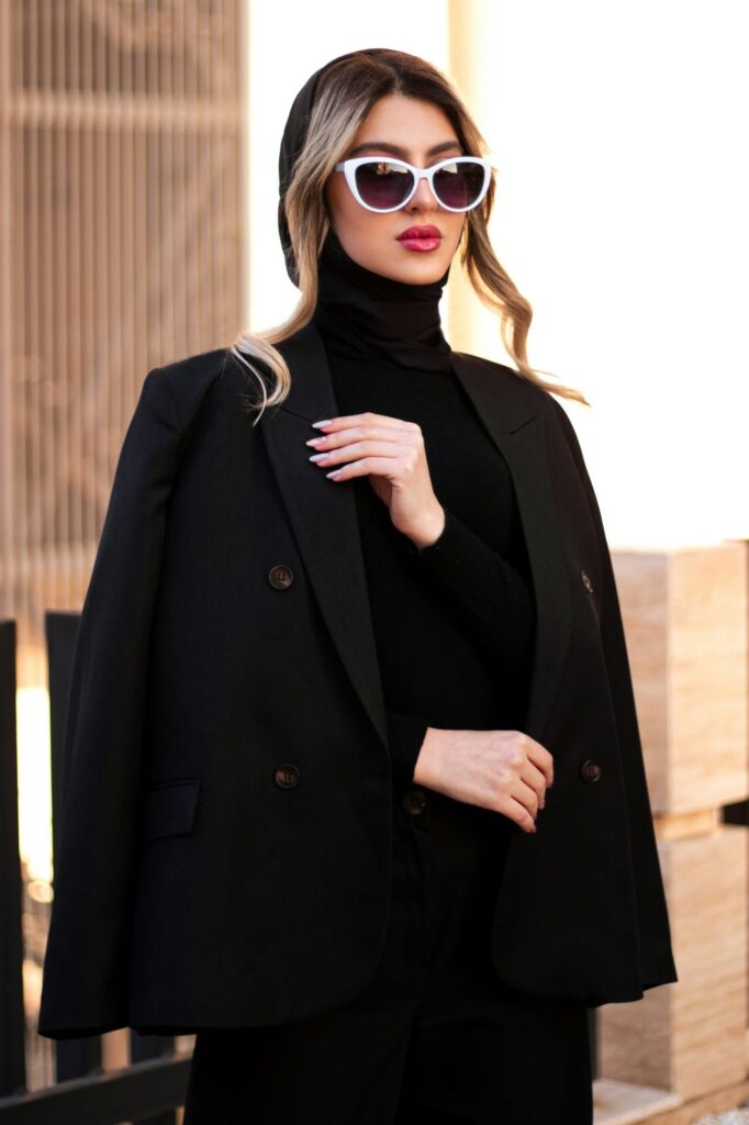 A woman wears a sleek black turtleneck with black peacoat and large white-framed sunglasses