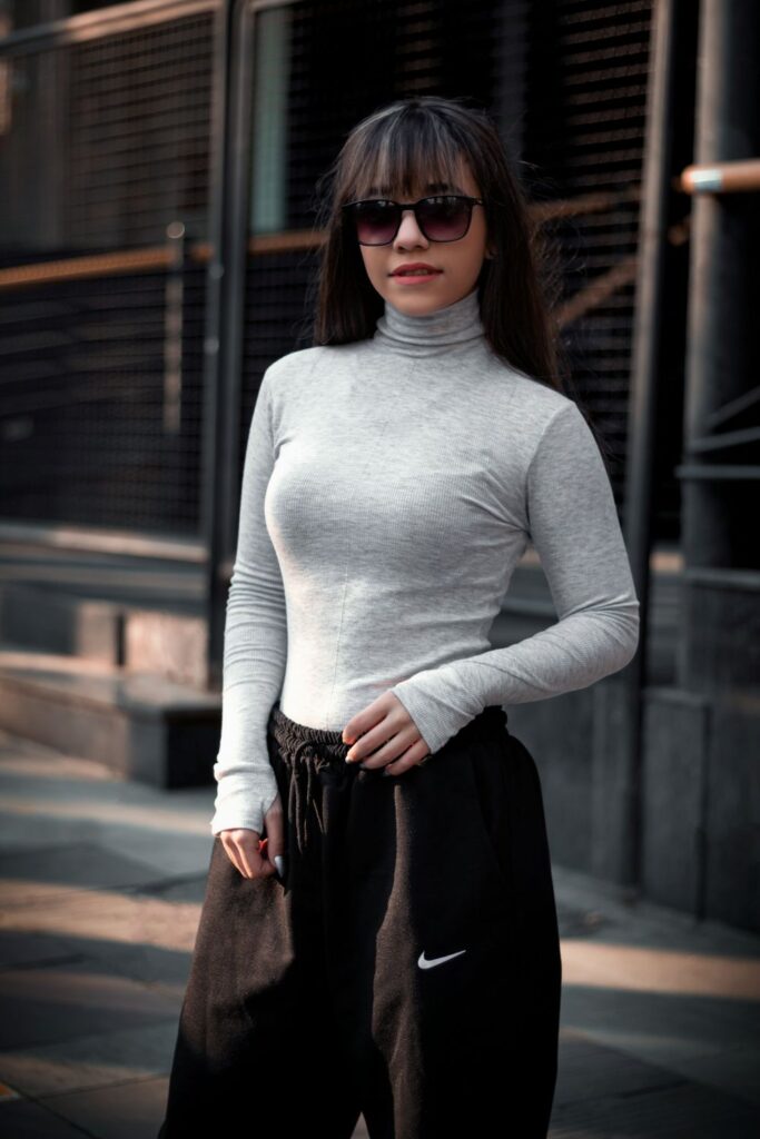 A woman in Tehran poses in a basic fitted gray turtleneck shirt, sunglasses, and Nike jogger pants - a fun example of 'put-together-casual' style