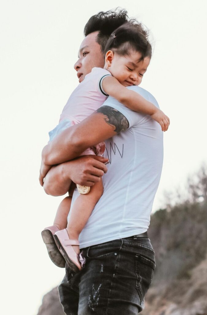 A dad holds a sleepy toddler in his arms in the wind