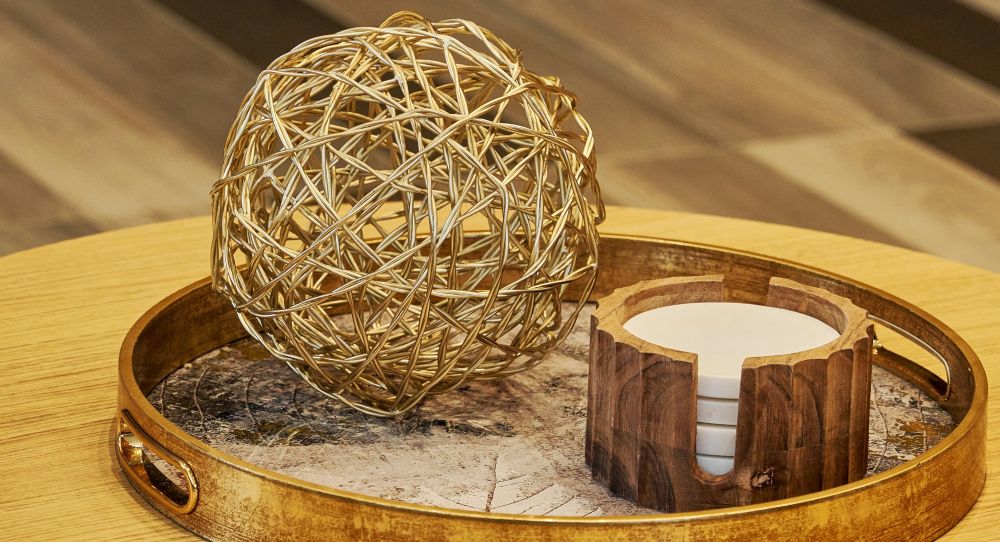Close-up photo of a decorative gold-coloured ball resting inside a round gold-brushed metal tray atop a round wood coffee table