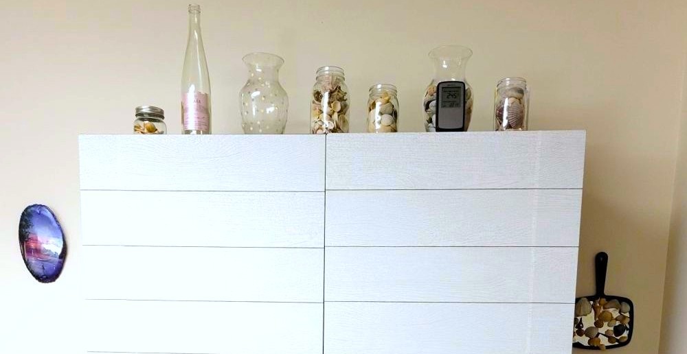 Cabinet with clear jars and vases filled with seashells on top. Filling clear vessels with favourite objects (read: free from nature!) is an excellent hack for decorating on a budget