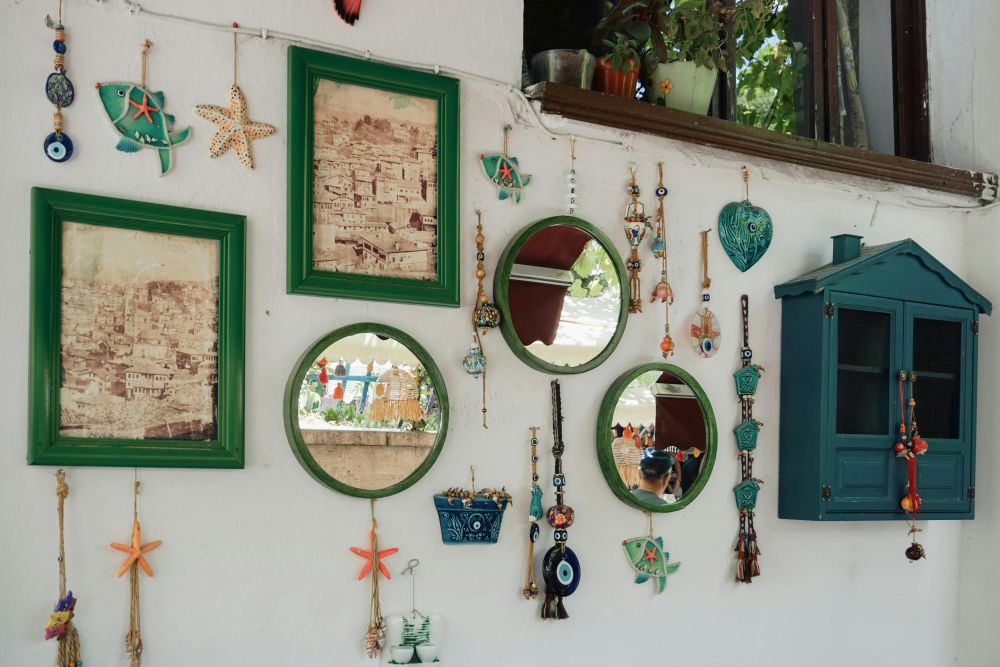 On a wall hangs many small mirrors among lots of lovely oceanic-themed and evil eye decorations in blues and teals