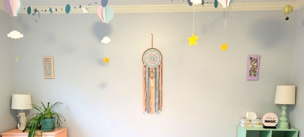 Decorating on a budget with pretty pastels: periwinkle and blue paper hot air balloons with hanging stars hang from a ceiling, with blue and silver paper star and circle garlands strung across the ceiling. A matching dream catcher hangs on th wall as well as framed seashell art.