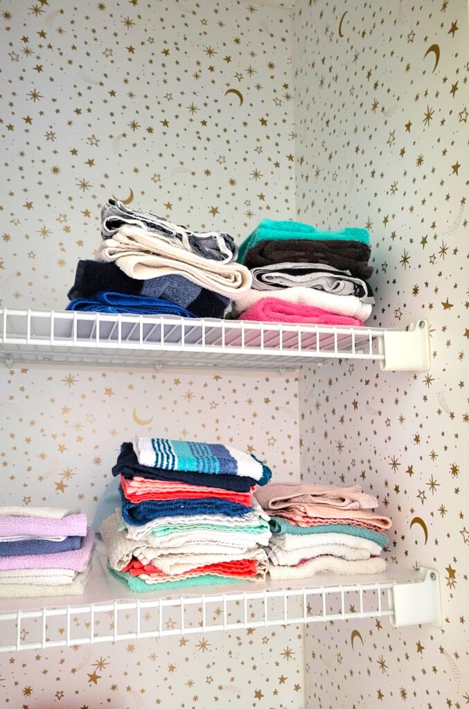 A linen closet with white peel-and-stick wallpaper covered in gold stars and moons. Decorating on a budget includes fun and playful touches to liven up even closets