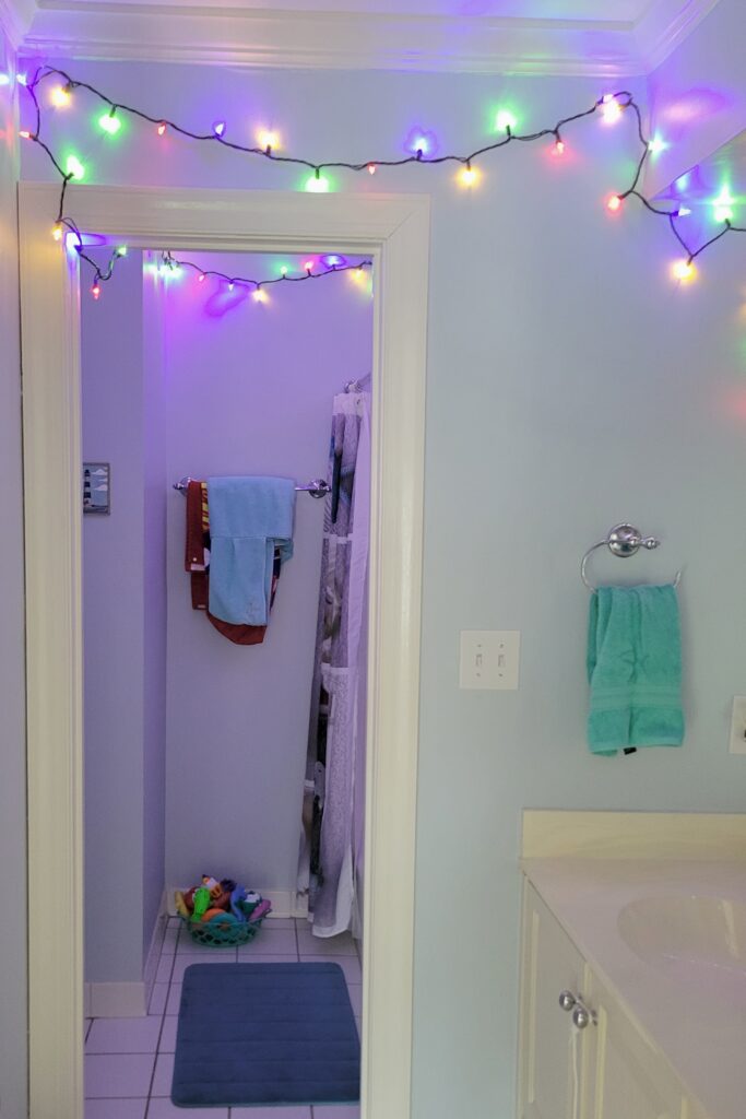 Multi-coloured string lights are strung across the ceiling of a bathroom, creating a cool and festive glow